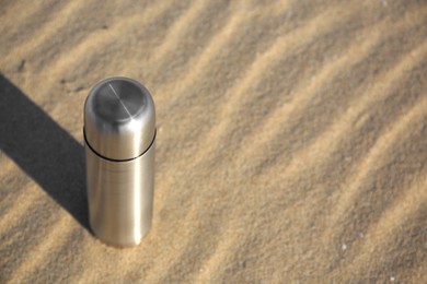 Metallic thermos with hot drink on sand, space for text