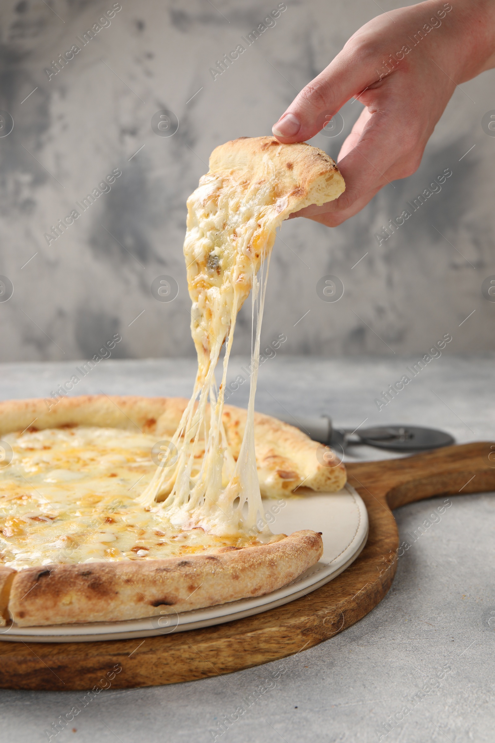 Photo of Woman taking piece of delicious cheese pizza at light grey table, closeup