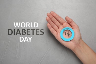 Image of Woman holding blue paper circle as World Diabetes Day symbol at grey table, top view 