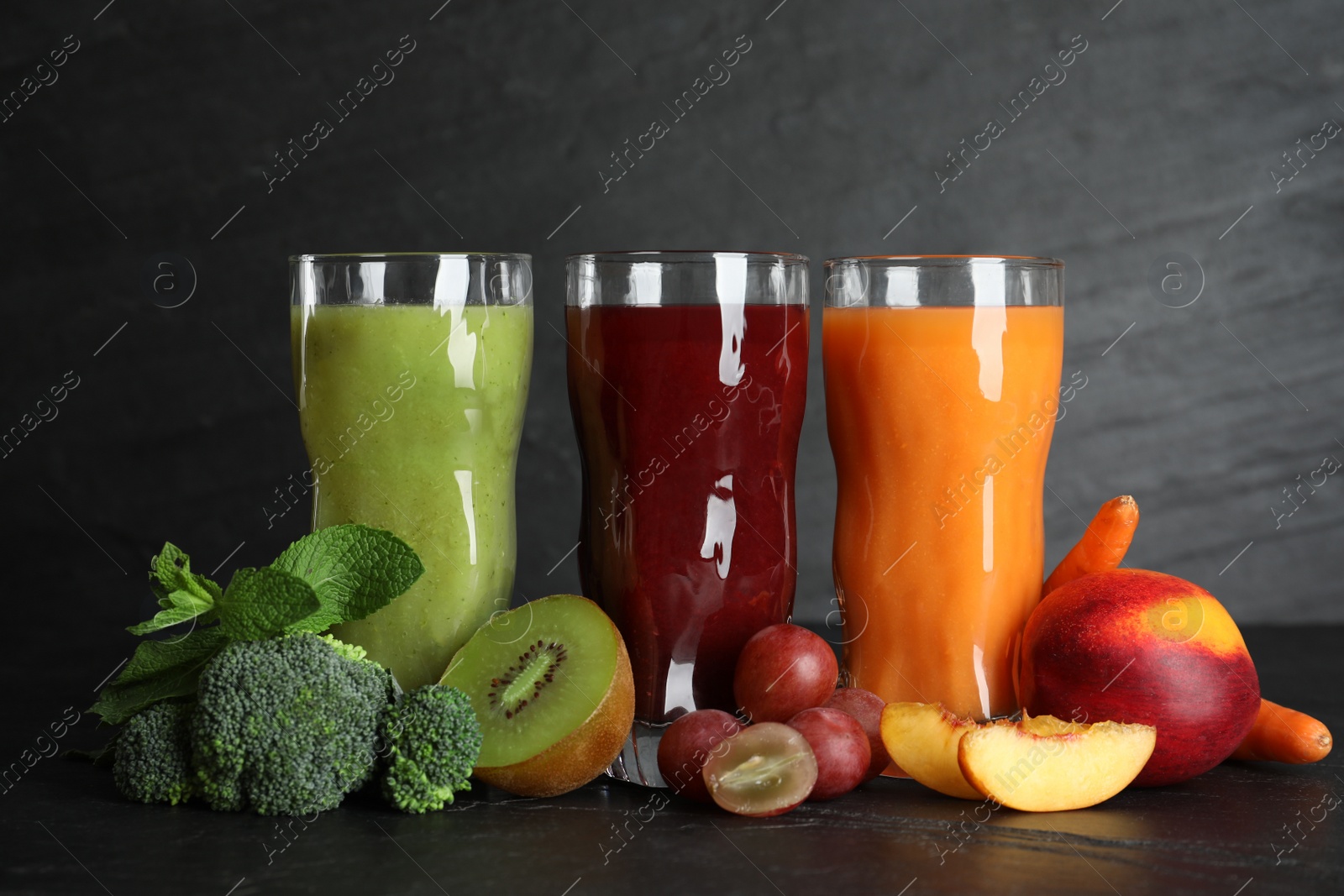 Photo of Delicious colorful juices in glasses and fresh ingredients on black table