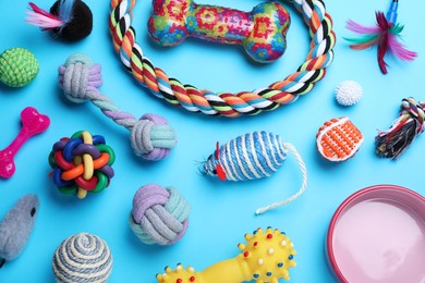 Different pet toys and feeding bowl on light blue background, flat lay