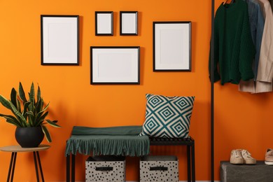 Empty frames hanging on orange wall in stylish room. Mockup for design