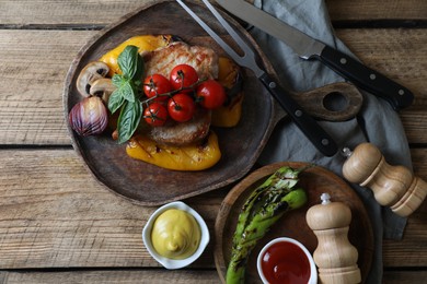 Photo of Delicious grilled meat and vegetables served with sauces on wooden table, flat lay