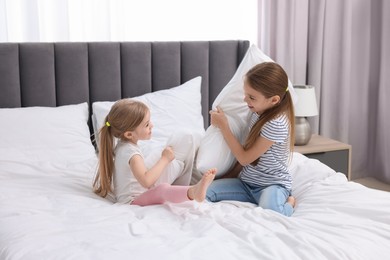 Cute little sisters having pillow fight on bed at home