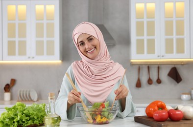 Muslim woman making delicious salad with vegetables at white table in kitchen