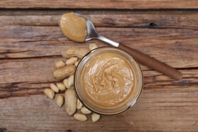 Tasty peanut nut paste in jar and spoon on wooden table, flat lay