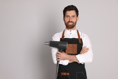 Photo of Smiling hairdresser wearing apron with dryer on light grey background, space for text