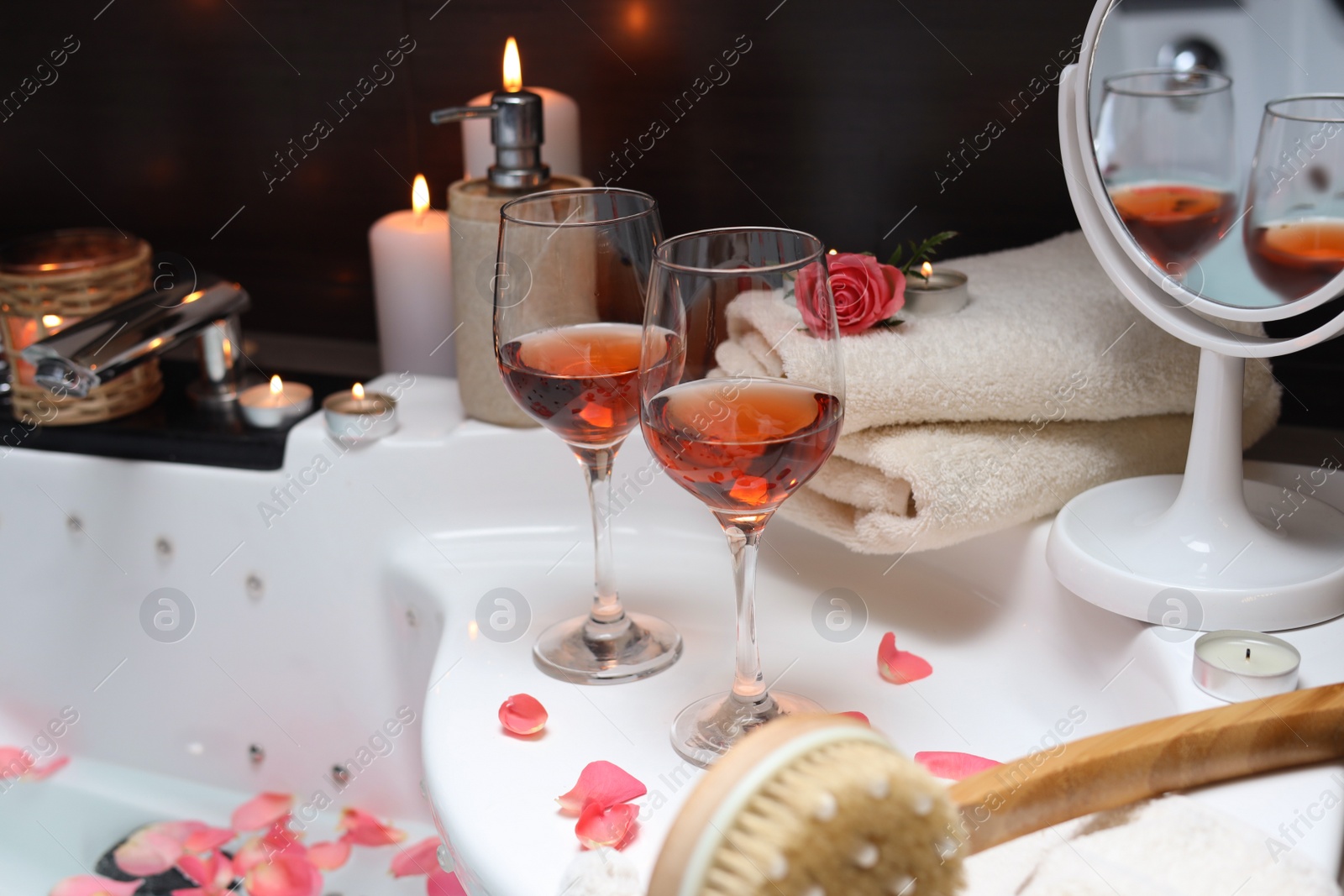 Photo of Bathtub with glasses of wine and candles indoors. Romantic atmosphere