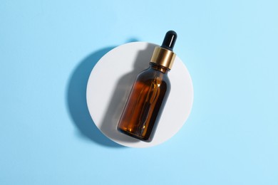 Bottle with cosmetic oil on podium on light blue background, top view
