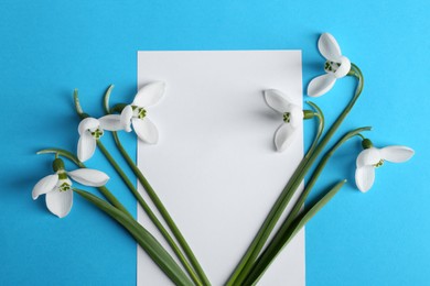 Beautiful snowdrops and card on light blue background, flat lay. Space for text