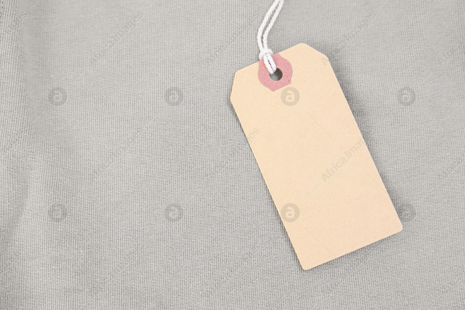 Photo of Cardboard tag on beige garment, top view. Space for text