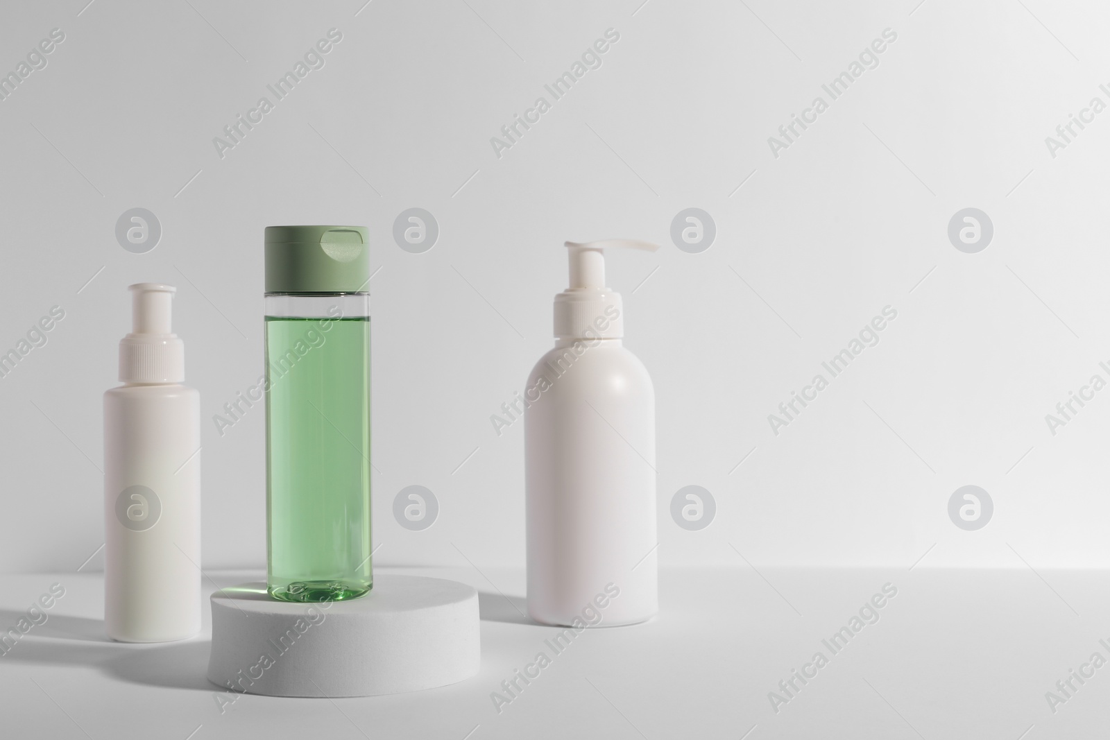 Photo of Bottles with different cosmetic products and podium on white background, space for text