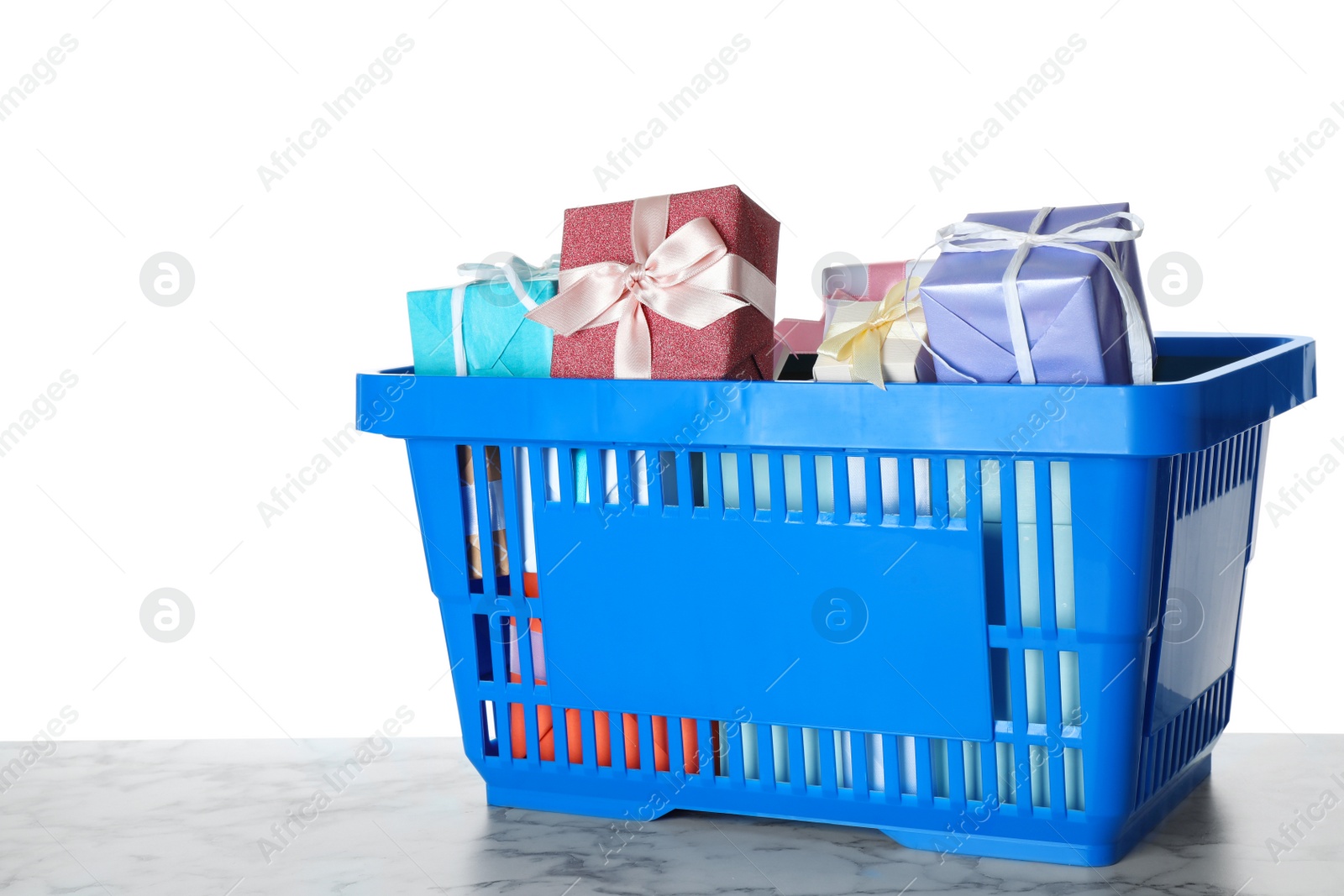 Photo of Shopping basket full of gift boxes on marble table against white background