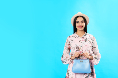 Photo of Young woman wearing floral print dress with stylish handbag on light blue background. Space for text
