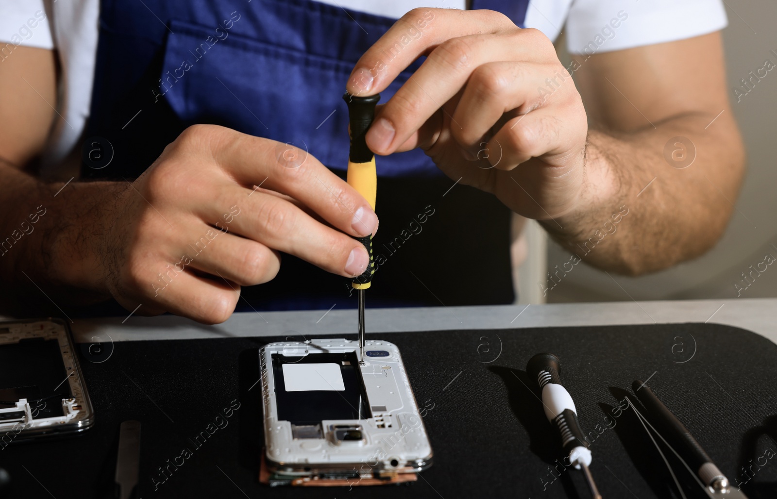 Photo of Technician repairing broken smartphone at table, closeup