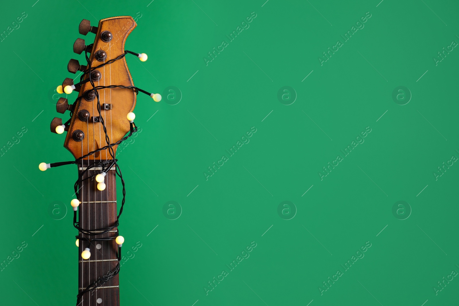 Photo of Closeup view of guitar with fairy lights on green background, space for text. Christmas music