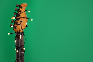 Photo of Closeup view of guitar with fairy lights on green background, space for text. Christmas music