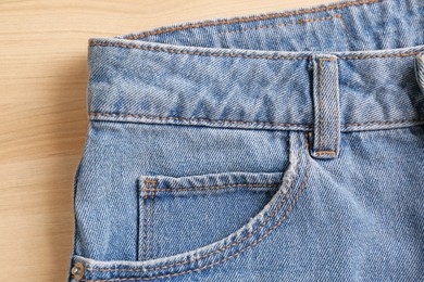 Photo of Stylish light blue jeans on wooden background, closeup of inset pocket