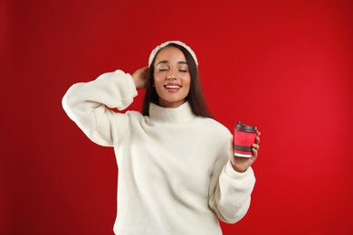 Photo of Happy beautiful woman with paper cup of mulled wine on red background