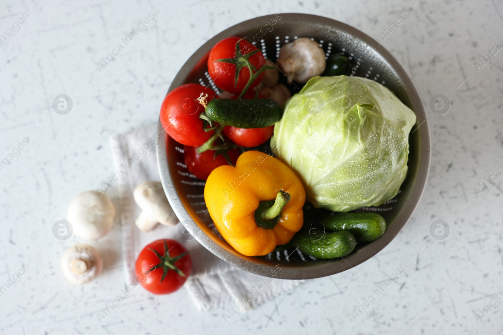 Photo of Metal colander with different wet vegetables on white textured table, top view