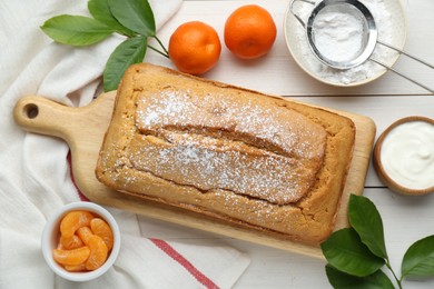 Photo of Delicious homemade yogurt cake with powdered sugar and tangerines on white wooden table, flat lay