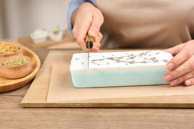 Photo of Woman cutting natural handmade soap on wooden table, closeup