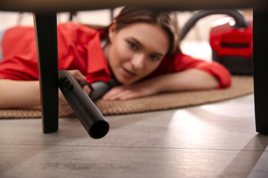 Photo of Young woman using vacuum cleaner at home