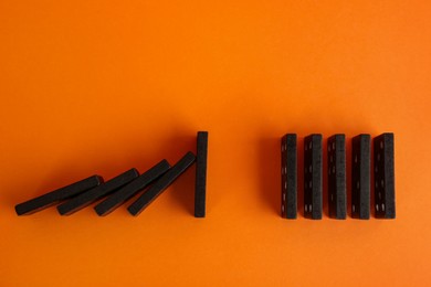 Photo of Black domino tiles on orange background, flat lay