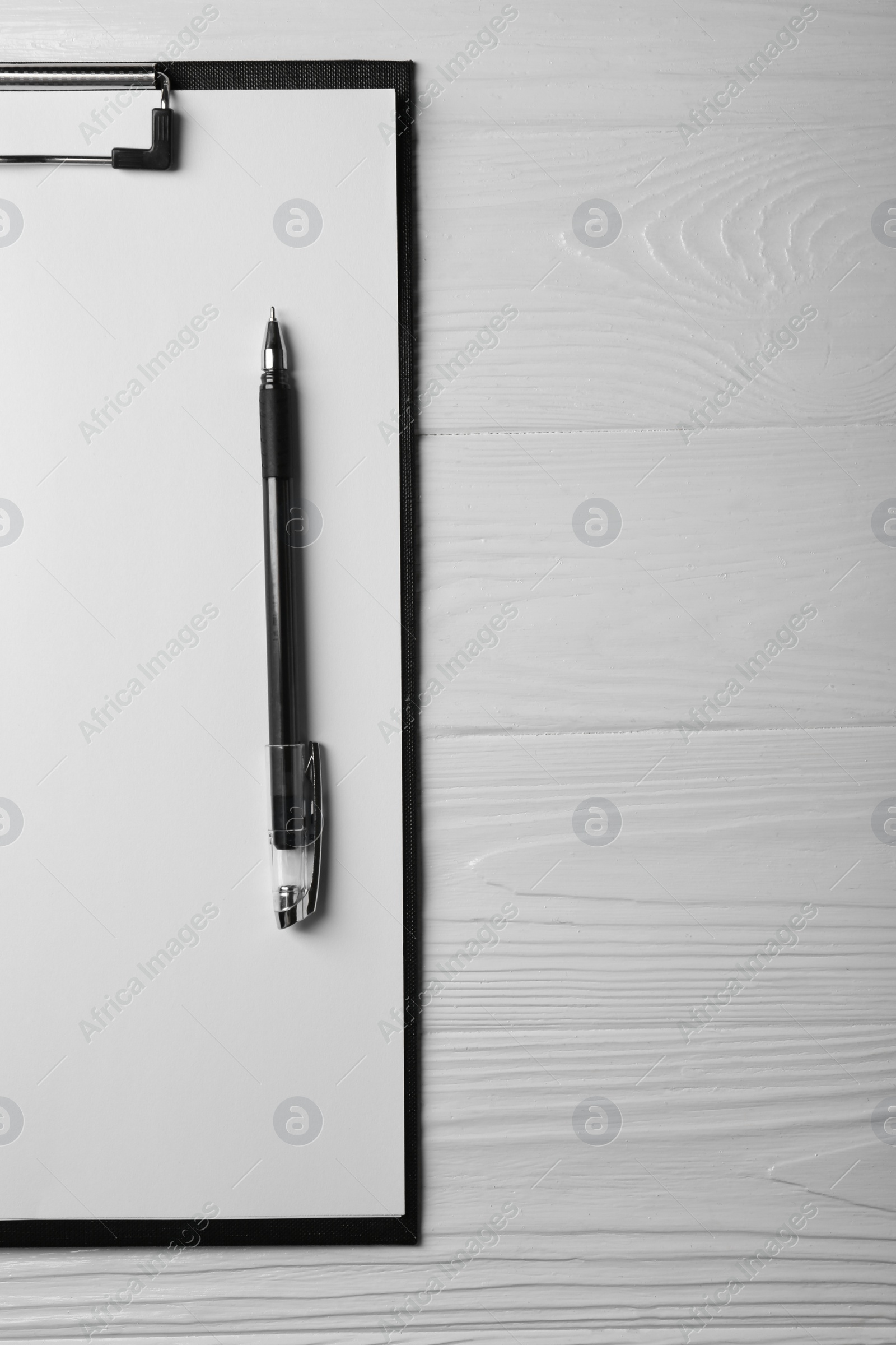 Photo of New clipboard with sheet of blank paper and pen on white wooden table, top view. Space for text