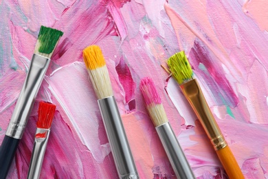 Photo of Set of different brushes on abstract colorful paint, flat lay