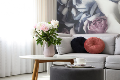 Bouquet of peonies on table near sofa in modern room. Interior design