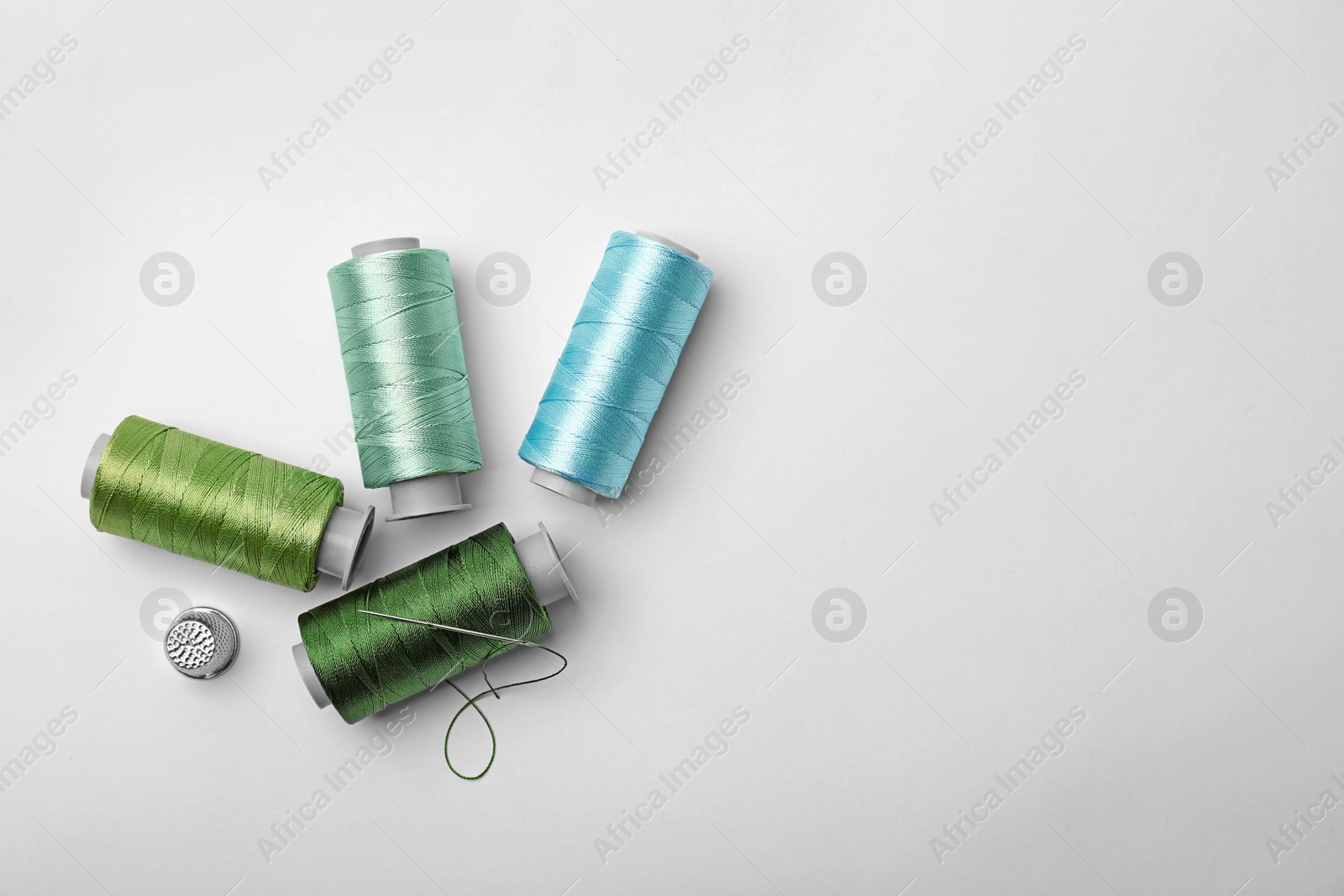 Photo of Color sewing threads and thimble on white background, top view