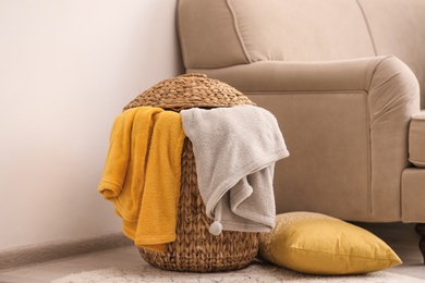Photo of Wicker basket with color blankets and pillow near beige sofa, space for text. Idea for interior design