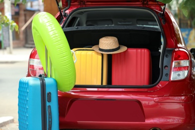 Photo of Car trunk with suitcases, hat and inflatable ring outdoors, closeup