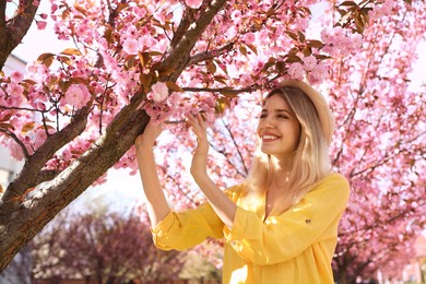 Photo of Happy stylish young woman near blossoming sakura tree outdoors. Spring look