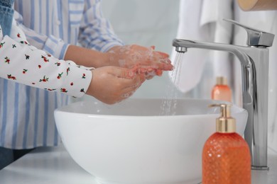Photo of Mother and daughter washing hands with liquid soap in bathroom, closeup