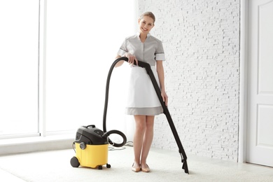 Photo of Chambermaid cleaning carpet with vacuum  indoors