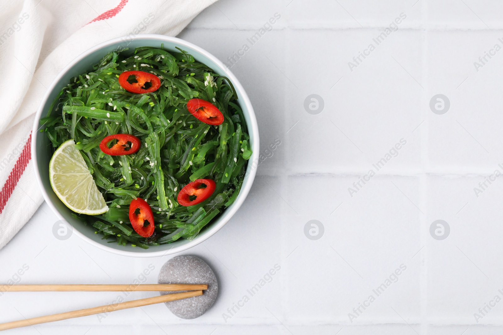 Photo of Tasty seaweed salad in bowl served on white tiled table, top view. Space for text