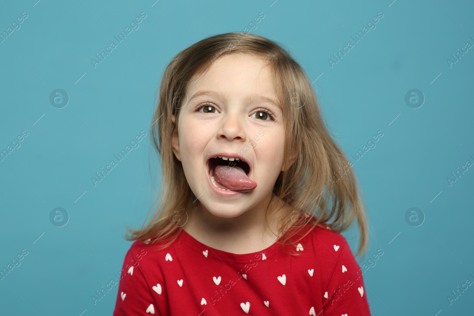 Photo of Funny little girl showing her tongue on light blue background