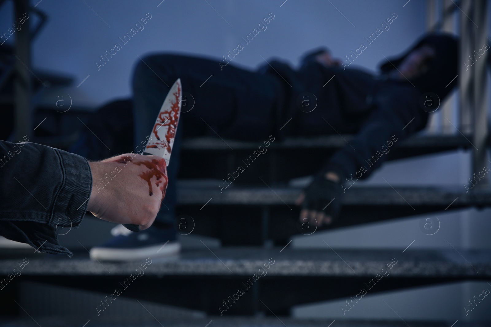 Photo of Man with bloody knife and unconscious person on stairs indoors, space for text. Dangerous criminal