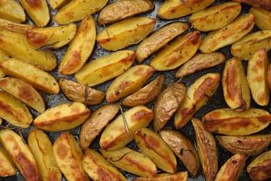 Photo of Delicious baked potatoes with rosemary on black surface, flat lay