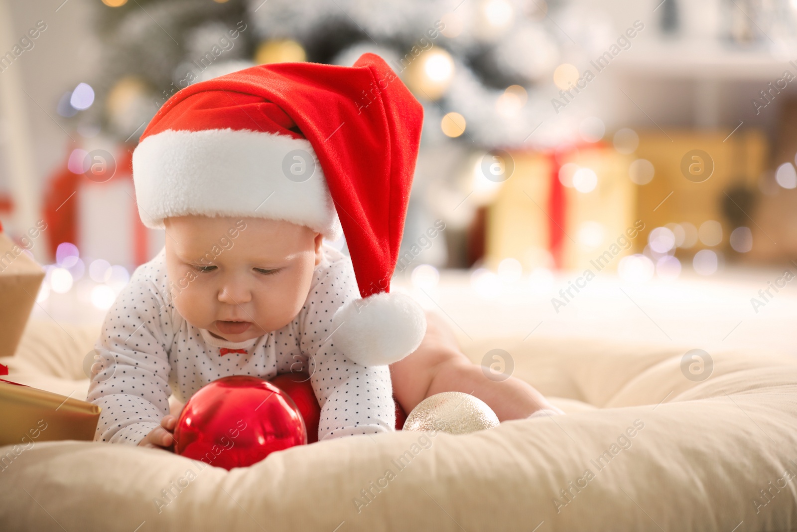 Photo of Little baby in Santa hat playing with Christmas balls indoors