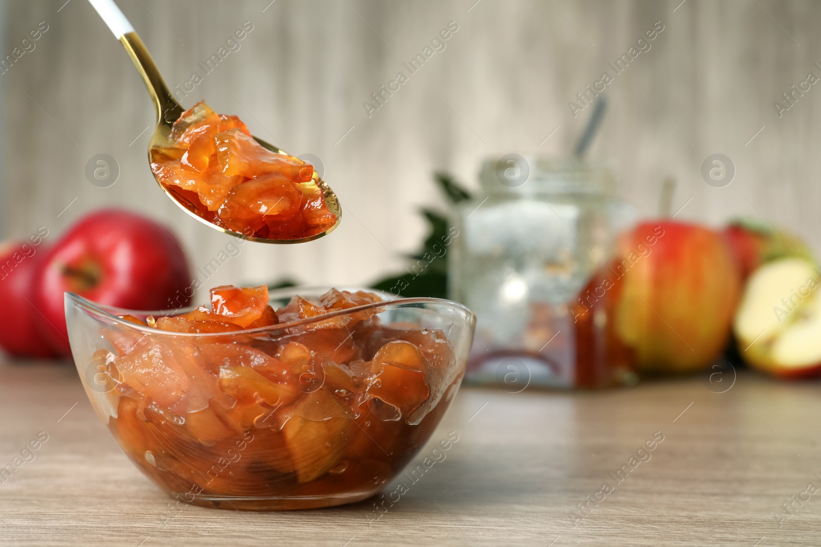 Photo of Spoon with tasty apple jam over glass bowl at wooden table, space for text