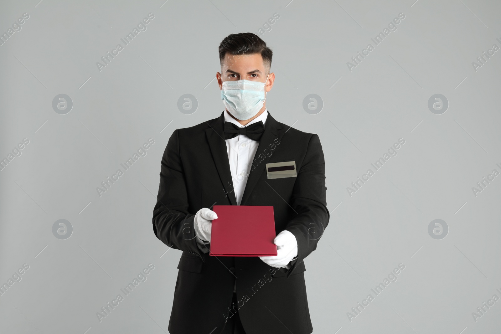 Photo of Waiter in medical face mask with menu on light grey background