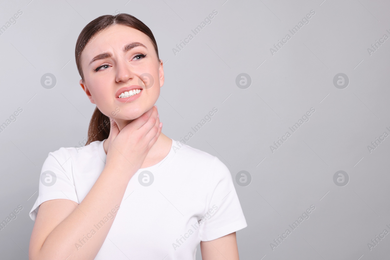 Photo of Young woman with sore throat on light grey background. Space for text