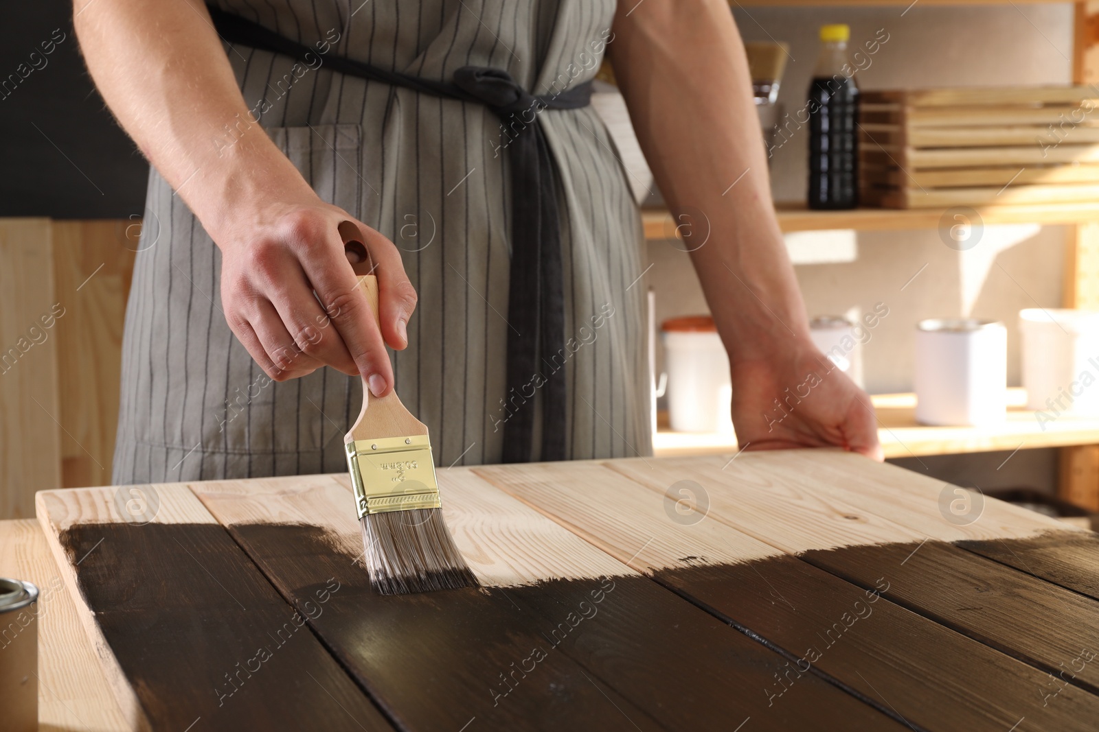 Photo of Man with brush applying wood stain onto wooden surface indoors, closeup