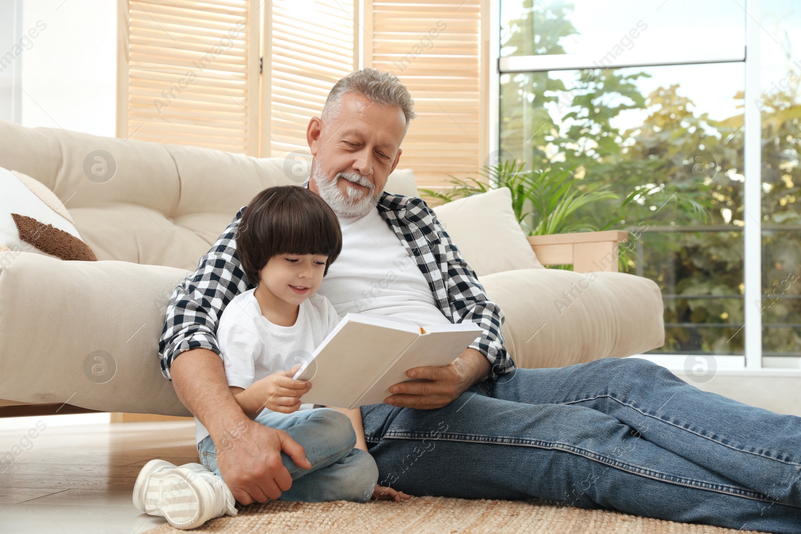 Photo of Happy grandfather with his grandson reading book together at home