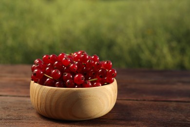 Photo of Fresh ripe red currant in bowl on wooden table outdoors. Space for text