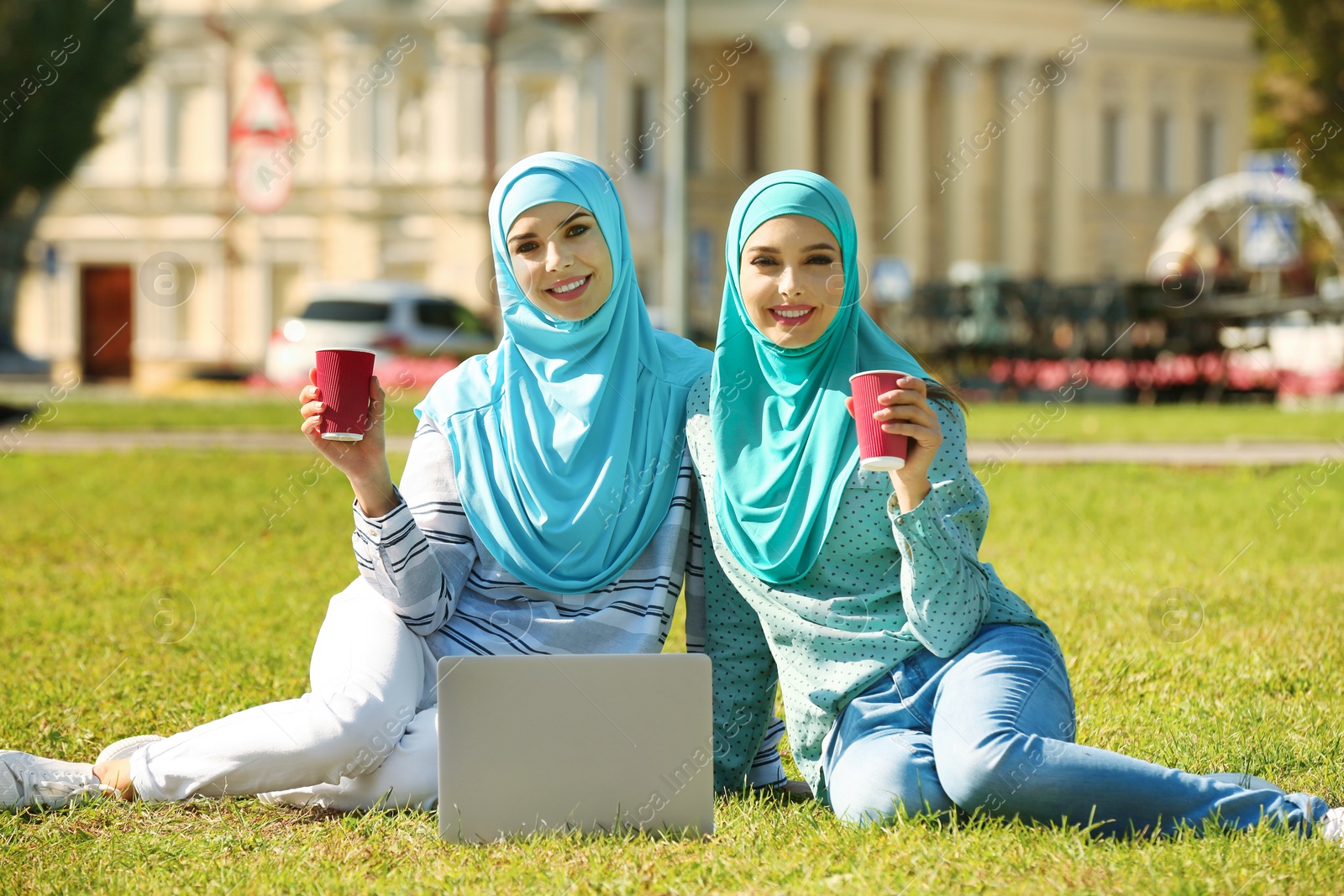 Photo of Muslim women in hijabs with laptop sitting on green lawn outdoors