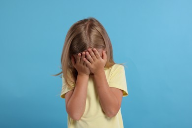 Resentful girl covering face with hands on light blue background